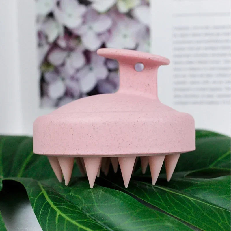 Pink scalp massager on a green leaf with a blurred floral background
