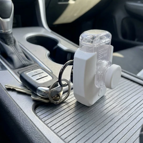 A white and clear handheld nebuliser shown on a keychain inside a car